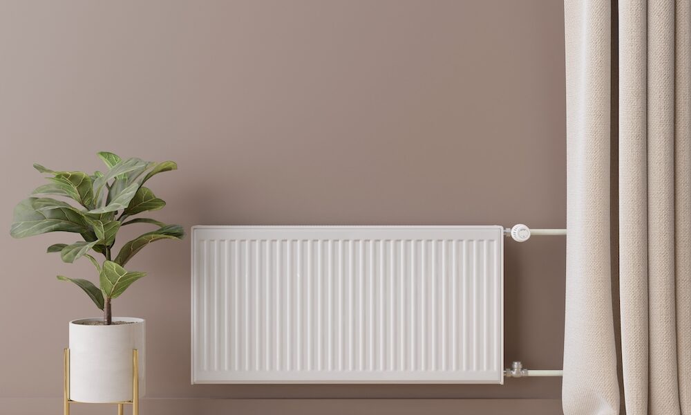 White heating radiator with thermostat on brown wall. Central heating system.