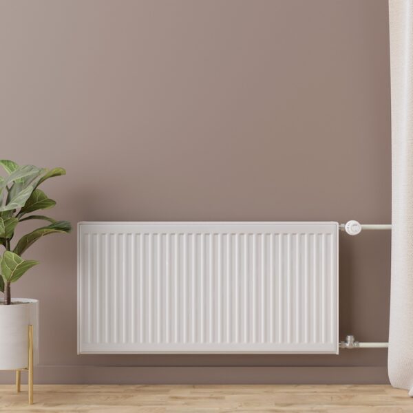 White heating radiator with thermostat on brown wall. Central heating system.