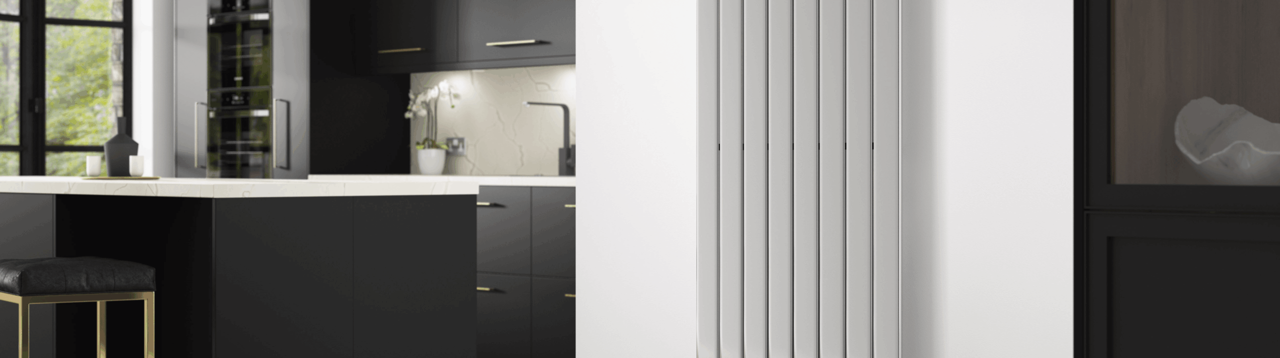 Modern kitchen interior featuring a tall vertical white radiator mounted on a wall beside sleek black cabinets, a marble countertop, and a bar stool with gold accents.